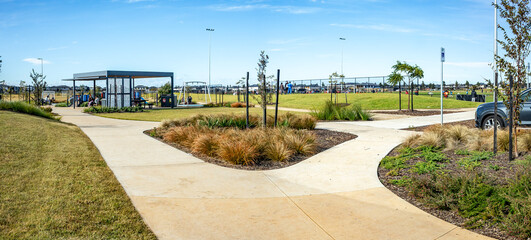 panoramic view of a landscaped suburban park in Australia, featuring curved concrete footpaths,...