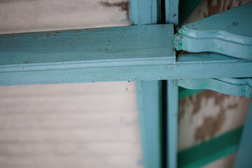 Close-up captures teal-painted architectural woodwork with water droplets clinging to the surface, showcasing weathered paint textures and an inviting glimpse of craftsmanship and design detail.