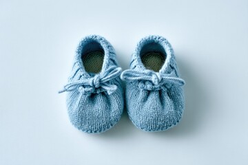 A pair of light-blue, hand-knitted baby booties with tiny bows rests on a pale background