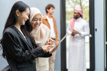 Muslim businesswoman in hijab discussing with asian colleague working on tablet in office, teamwork...