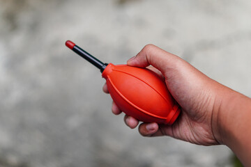 Close-up of hand holding a red air blower, a tool for removing dust and debris, presented against a...