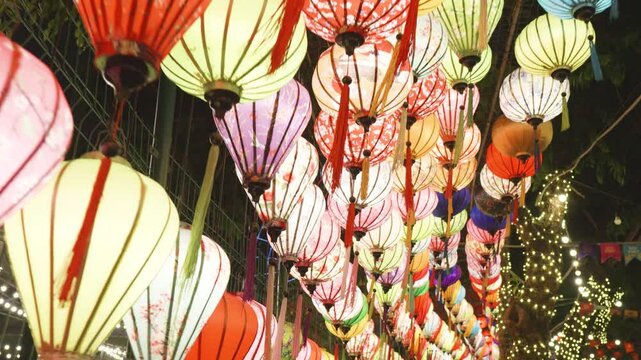 Multicolored paper lanterns hanging from overhead wires, illuminating evening festivity with soft, warm glowing light