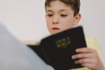 A boy is reading the holy bible and praying or meditating. Concept of Christianity, religion and faith.
