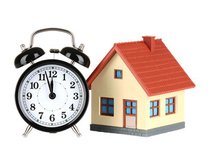 Classic Alarm Clock beside a Small House Miniature with Red Roof and Windows Showing Time Concept