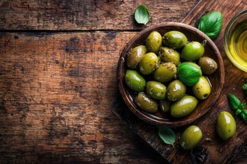 A rustic wooden surface displays a bowl of marinated green olives, garnished with basil, alongside a small dish of olive oil and scattered leaves