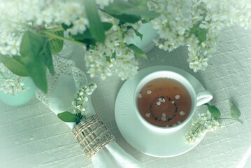 Cup of tea on the table with spring fresh bouquet with white blooming fragrant branches of bird...