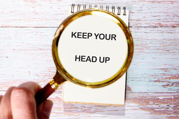 Concept words KEEP YOUR HEAD UP cognized with a magnifying glass in a blank notebook