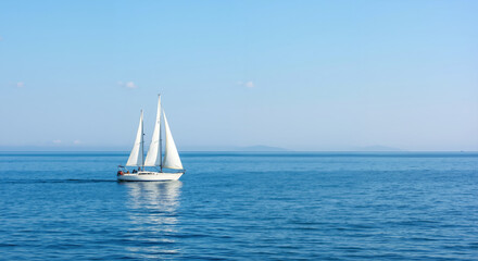 Fototapeta premium White sailboat with raised sails floating on calm blue sea under clear sky. Summer maritime adventure and tranquil ocean journey for travel agency promotions