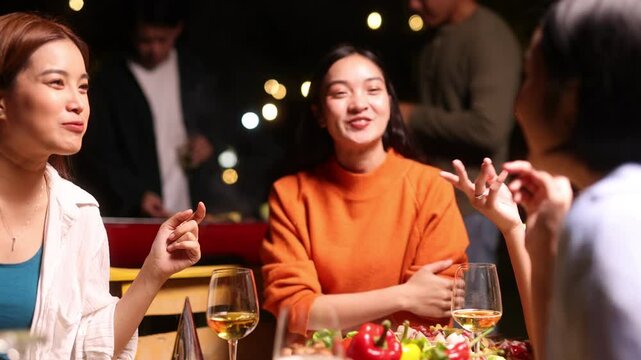 Friends toasting and enjoying drinks at a night party. Friends gathering for joyful nighttime celebration, food under warm string lights, sharing laughter and festive moments together.
