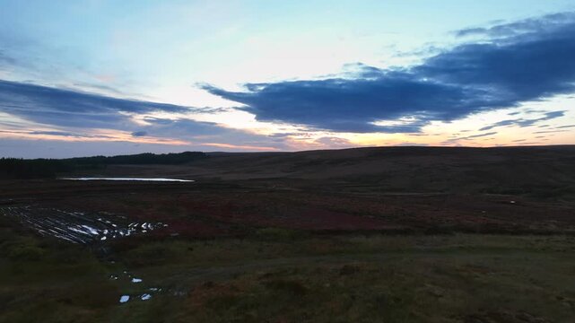 Bragan, County Monaghan, Ireland, September 2022. Drone low aerial dolly over bog landscape with small puddles appearing between grasslands with winding streams as dusk glow illuminates horizon.