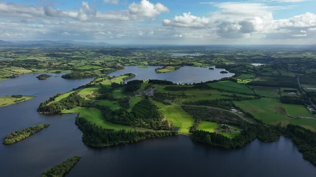 Lough Muckno, County Monaghan, Ireland, September 2022. Drone panoramic high angle aerial approach over cloudy landscape with s unlight illuminating water and countryside.