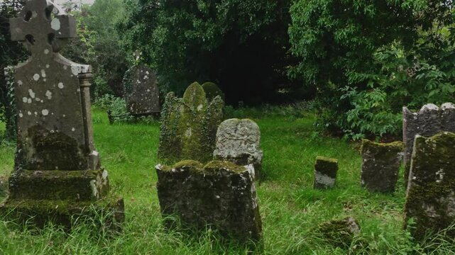 Old Donagh Graveyard, County Monaghan, Ireland, September 2022. Drone tracking left closeup backdrop of thin historic tomb and headstones in tall grass field, slow motion backdrop.