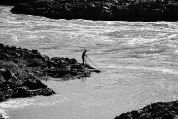 Black and white photo of a man fishing by the river in Iceland