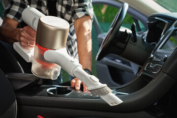 Man is vacuuming dirty car interior using handheld cordless vacuum cleaner. Car owner care about...