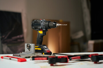 Electric cordless drill with bits and hand tools on workbench in workshop. Home renovation,...