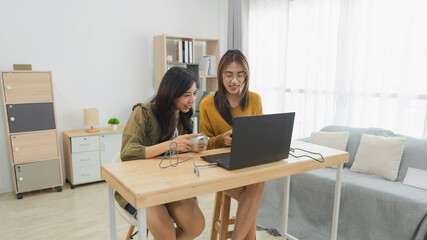 Two Young Women Enjoying Leisure Time Playing Games on Laptop in Bright Modern Room with Minimalist...