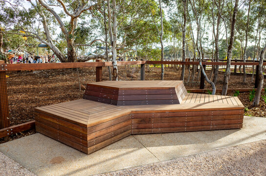 Contemporary multi-level wooden bench with a geometric design in a landscaped bushland park in Australia. Surrounded by eucalyptus trees,offers seating for visitors in a shaded natural environment.