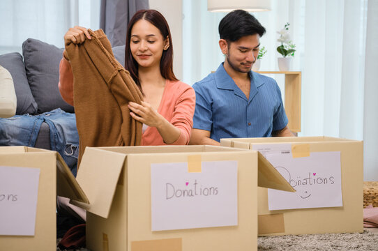 group of friend  sorting and packing clothes into a donation box.community support, and charitable giving - Powered by Adobe