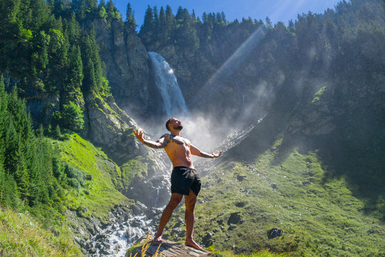 Carefree man in waterfall. Man freedom in waterfall landscape. Muscular man breathing fresh air on beauty waterfall. Topless model with raised hands on mountain nature landscape. Yoga by waterfall.