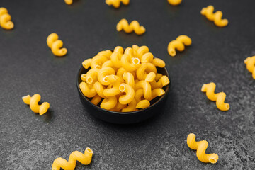 Curved pasta shapes arranged around a bowl on a dark surface