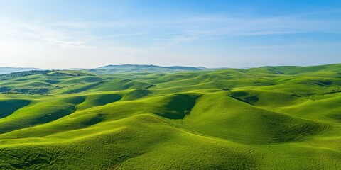Obraz premium An aerial view of endless rolling hills covered in green grass under a bright blue sky