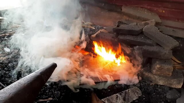 Close-up of steel being heated in a traditional Indonesian blacksmith forge with open fire and charcoal. Old-style metalworking process