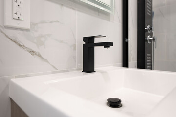 Modern black faucet on a clean white sink in a bathroom with marble tile. Stylish and minimalist...