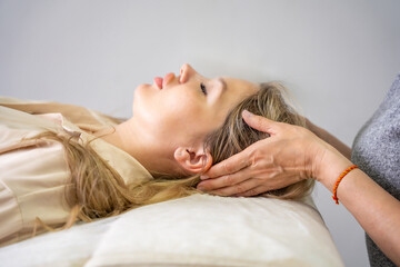 Female practitioner performs facial lifting technique on a young woman lying on a couch. Concept of...