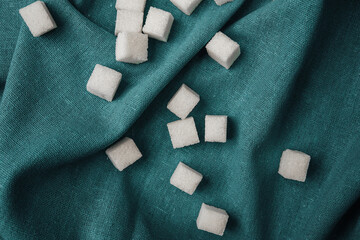 Small sugar cubes scattered on a teal fabric surface in a cozy kitchen setting
