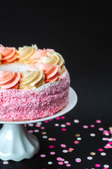 Pink and cream layered cake on a stand with colorful confetti