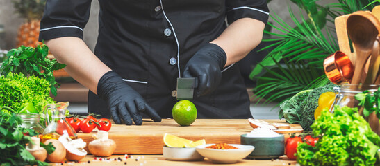 Cooking food in the kitchen. Chef is going to cut lime. Wooden table, kitchenware, vegetables, herbs and ingredients. Healthy vegan eating, recipes, blogging