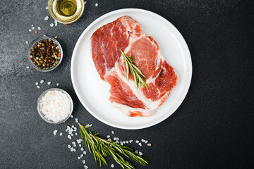 Uncooked beef steaks on white plate with rosemary and spices