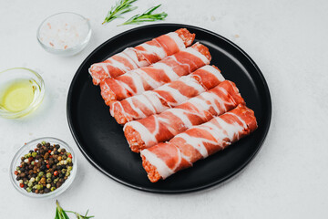 Bacon wrapped sausages on black plate with spices and rosemary