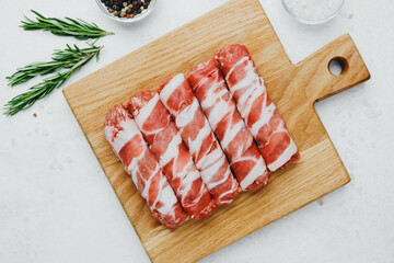 Sausage rolls wrapped in bacon on wooden board with herbs