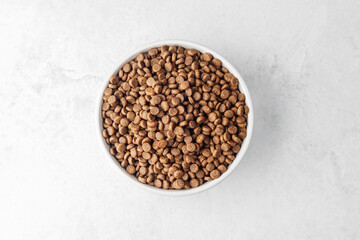 Bowl of dry dog food placed on white textured background from top view