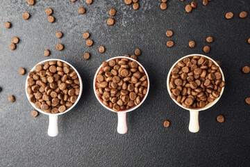 Three bowls of dry dog food on black textured background with scattered kibble