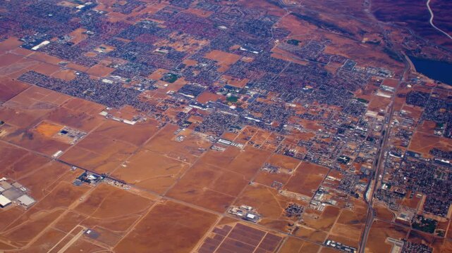 Aerial view of a sprawling suburban grid interwoven with roads, farmland, and industrial areas, highlighting the contrast between urban development and arid, undeveloped land.