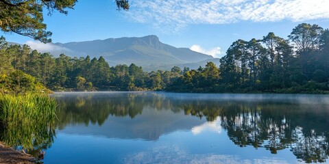 A tranquil mountain lake with mist hovering above the water, reflecting the trees and sky