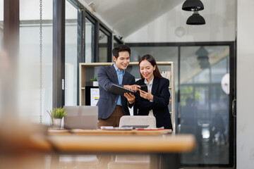 Team of Young business Asian man and woman using using tablet computer standing near the window in workplace	