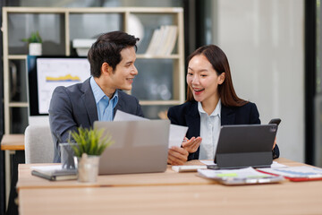 Fototapeta premium Young Asian Man and Woman manager project on laptop in modern office. Two business people of professional working, studying, writing notes sit at desk 