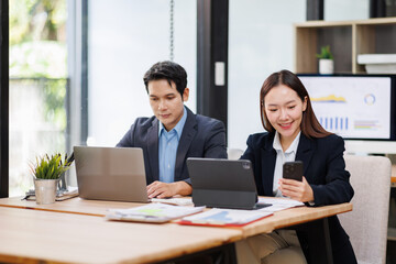 Fototapeta premium Young Asian Man and Woman manager project on laptop in modern office. Two business people of professional working, studying, writing notes sit at desk 