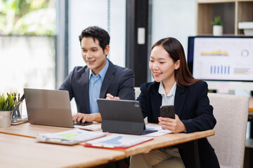 Young Asian Man and Woman manager project on laptop in modern office. Two business people of professional working, studying, writing notes sit at desk 
