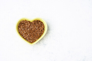 Flax seeds in a heart-shaped bowl on a marble surface