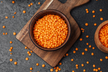 Bright orange lentils in a wooden bowl on a dark textured surface