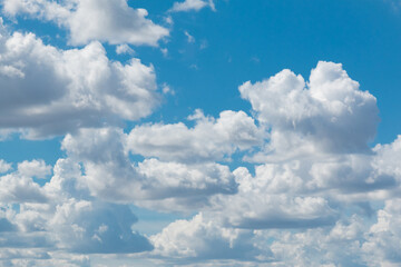 White fluffy clouds scattered across a vibrant blue sky, creating a serene and peaceful atmosphere. The clouds appear soft and majestic, adding depth to the sky's texture