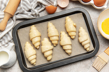 Baking tray with raw croissants, waiting to be cooked, surrounded by kitchen utensils