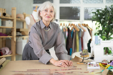 Mature fashion designer drawing sketch on paper. dressmaker makes markings and creates patterns of...