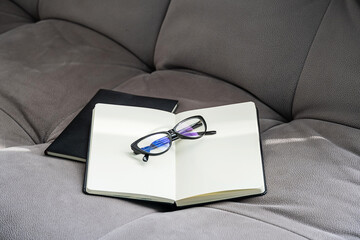 Open Notebook with Blank Pages and Pair of Glasses Rests on a Gray Couch.