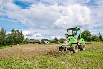 Mini skid steer loader clear a construction site. Small tractor with a ground leveler moves soil. Land work by the territory improvement, plot leveling. Plowing agricultural field. High quality photo.