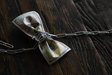 Financial Constraint: Chains Restricting Hundred Dollar Bills Tied with Paperclips on Dark Wood...